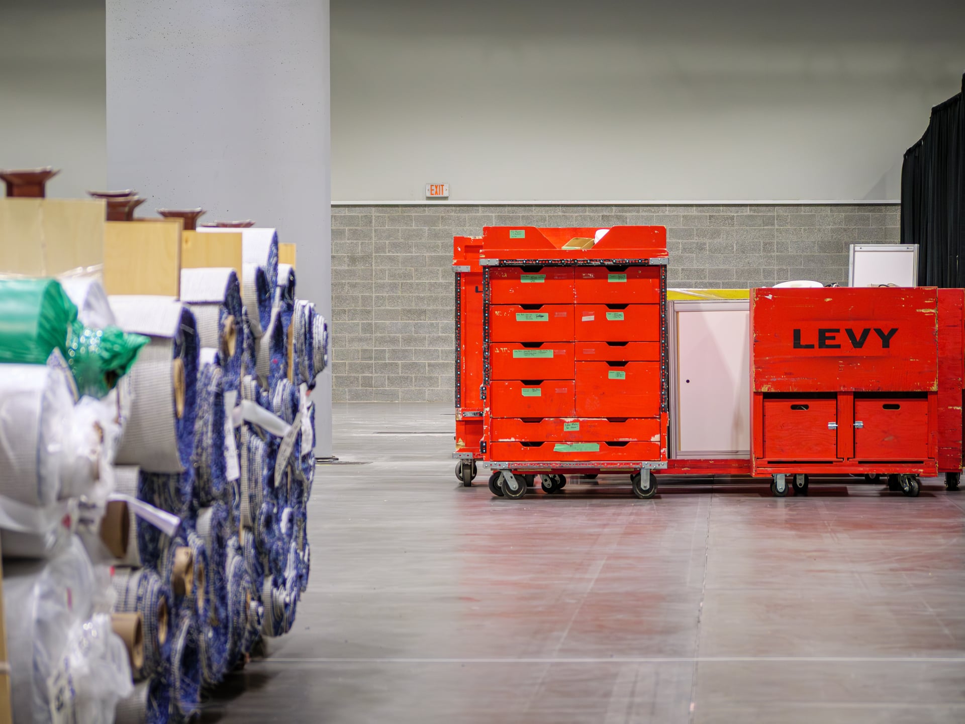 LEVY-branded red equipment carts and rolls of show carpet staged behind a venue’s concrete pillar, ready for the next move-in.