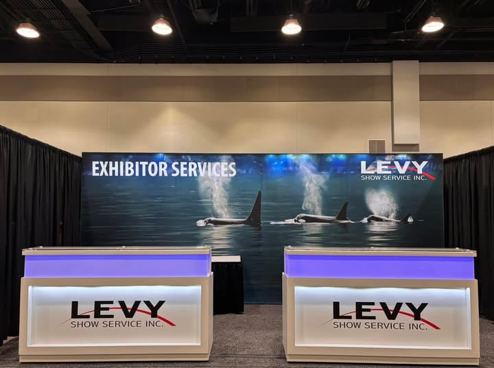 Two illuminated LEVY Show Service counters in front of the Exhibitor Services orca backwall.