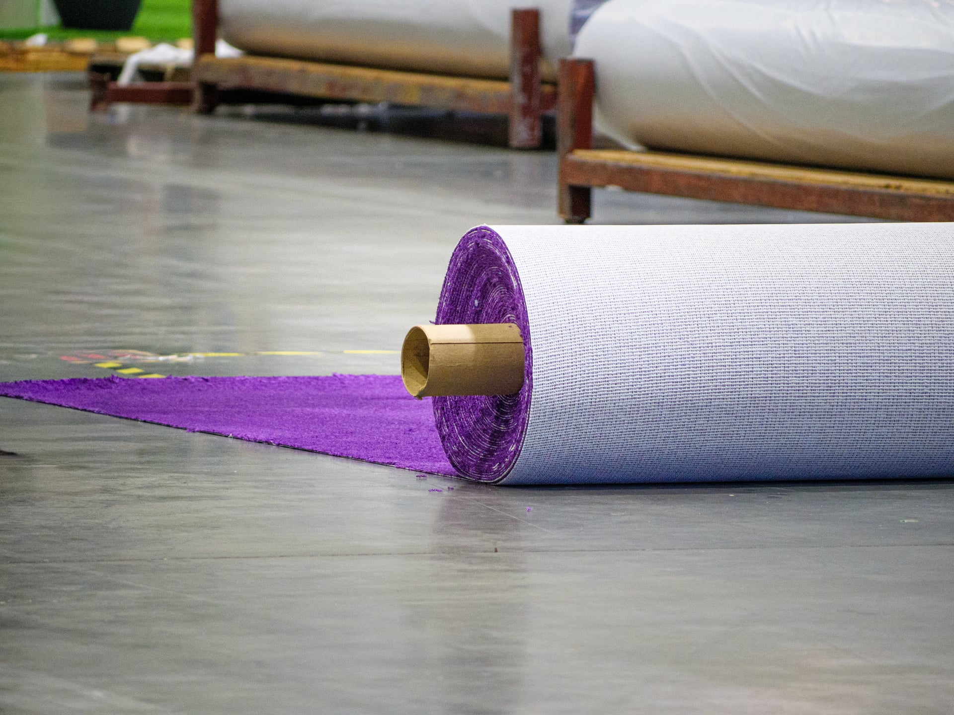 A roll of purple show carpet being rolled out across the polished concrete of an empty show floor.