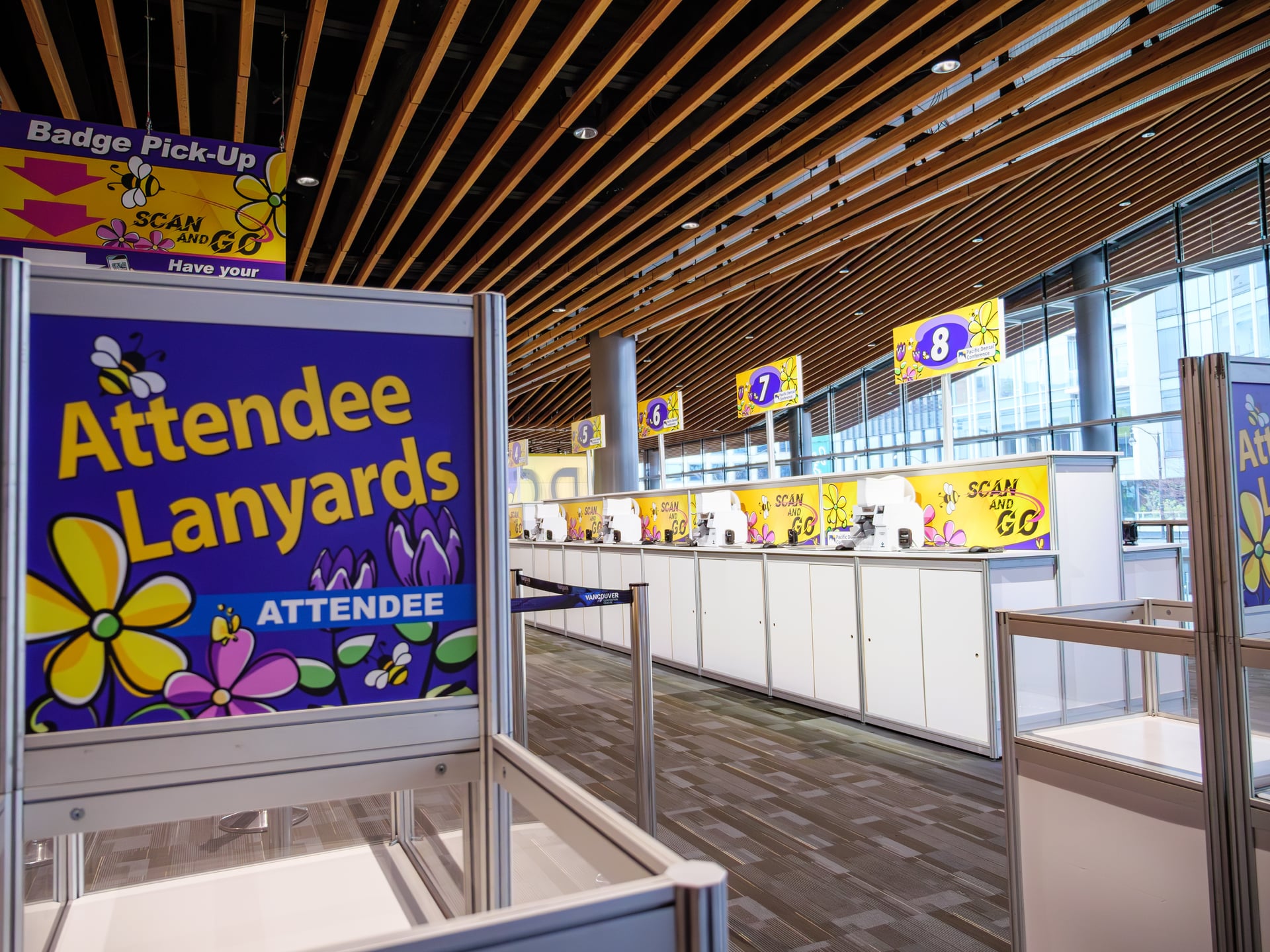 Pacific Dental Conference attendee badge pickup, complete with brightly branded numbered stations and the distinctive wood-slat ceiling of the Vancouver Convention Centre.